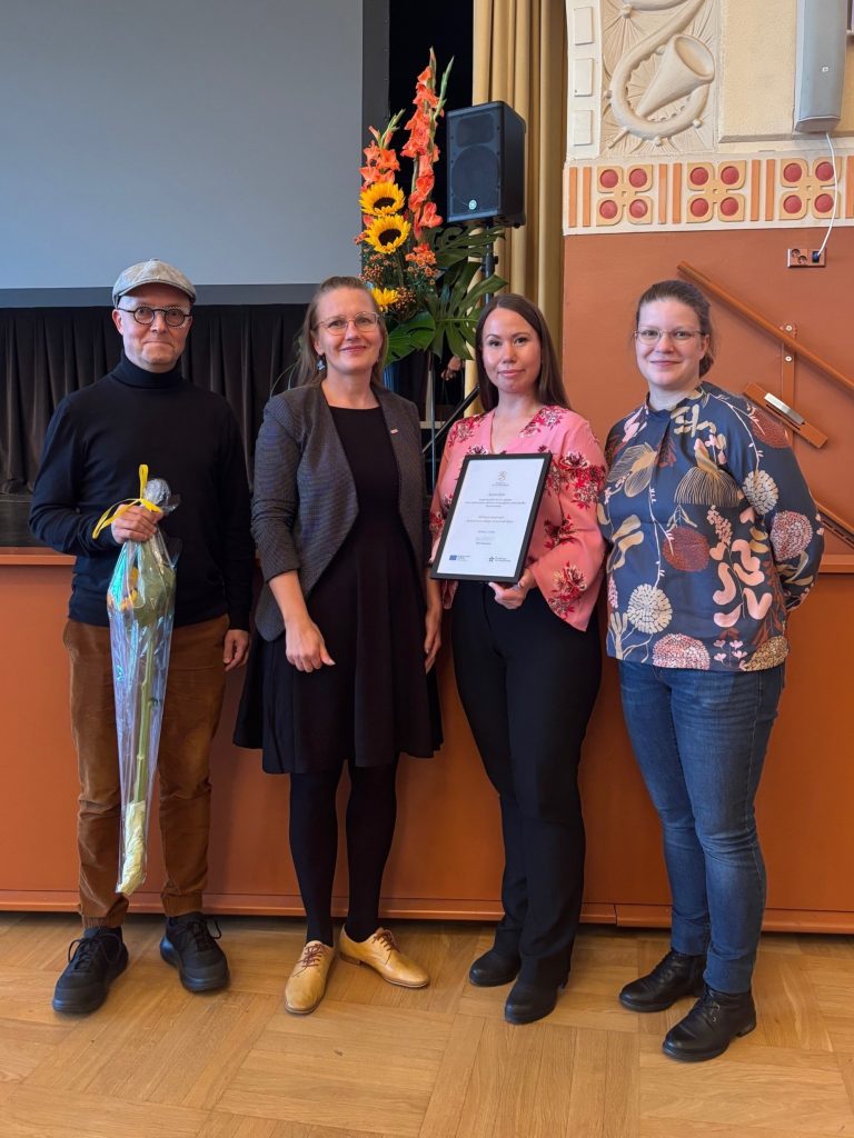 Kuvassa hanketiimin jäseniä kunniakirjan ja kukkapuskan kanssa.