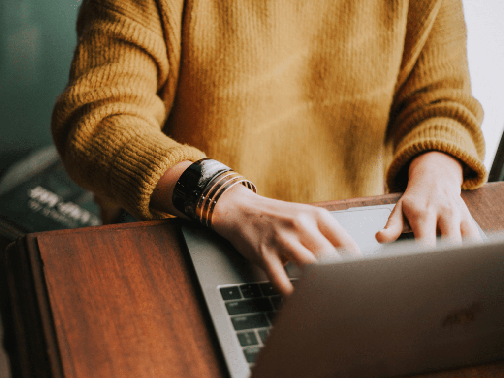 Keltapaitaisen ihminen istuu työskentelemässä kannettavan tietokoneen ääressä.