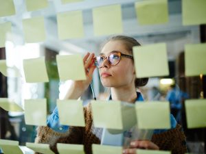 Kuvassa nainen tarkastelee lasiseinällä olevia muistilappuja