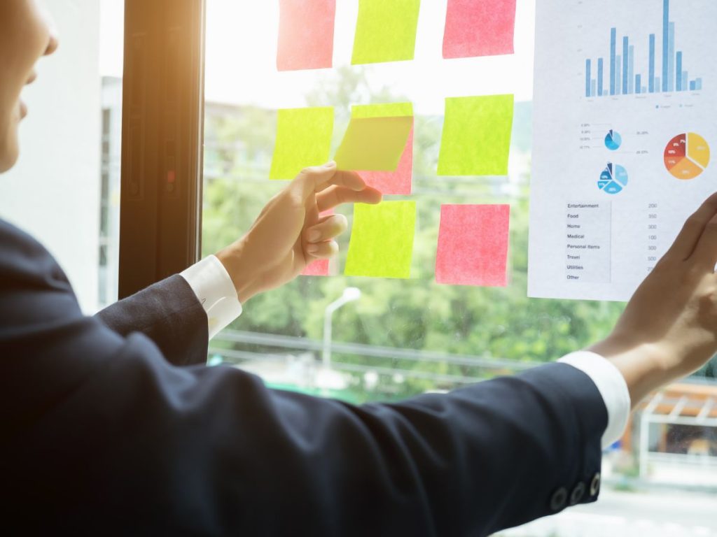 Kuvassa henkilö katselee ikkunaan kiinnitettyjä muistilappuja sekä kaavioita.