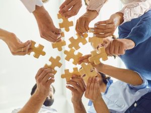 Kuvassa useat kädet tuovat yhteen palapelin palasia.